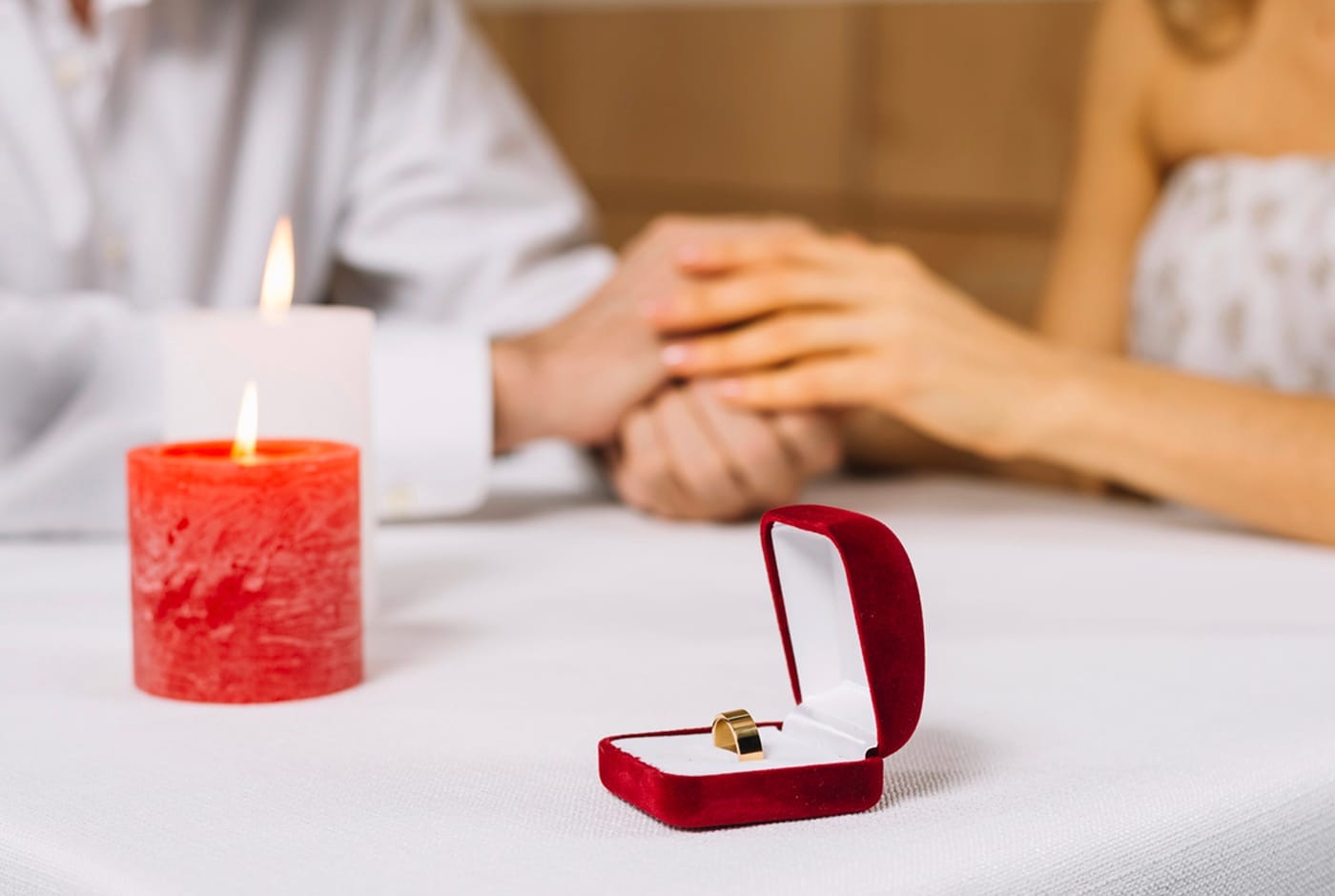 Couple holding hands at a candlelit table with an engagement ring in a box